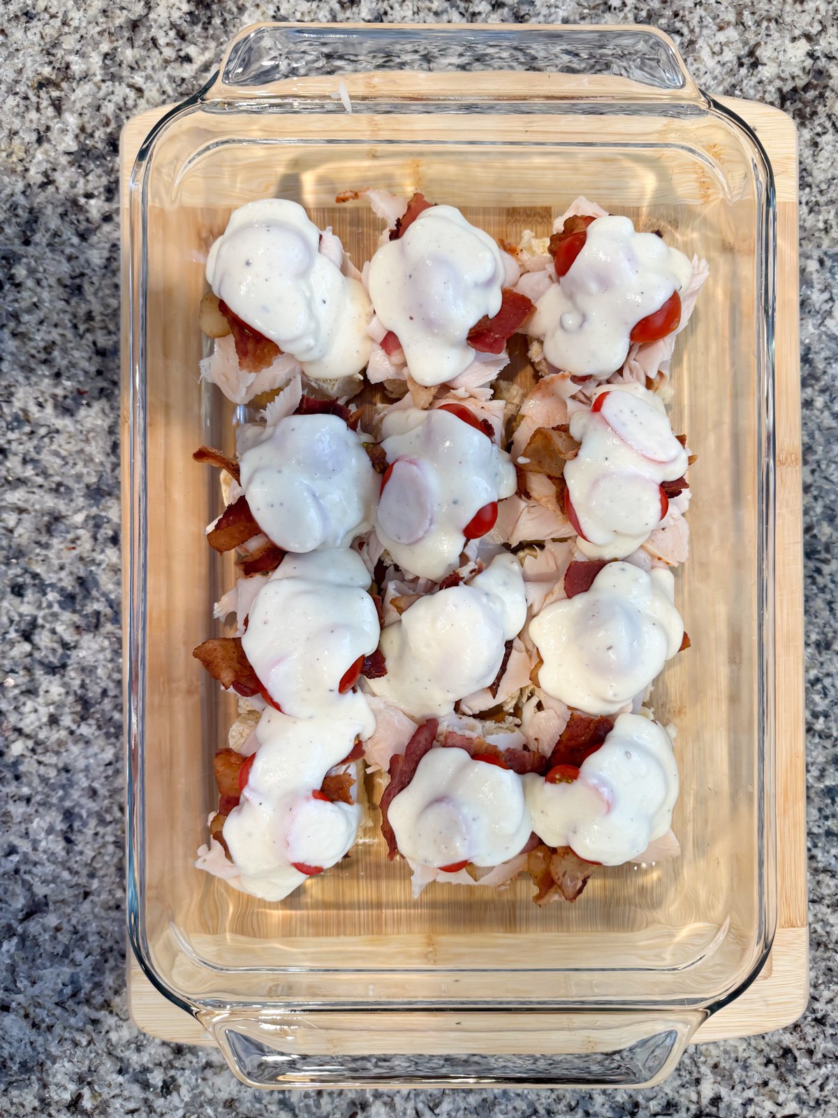 Adding mornary sauce to the tops of sliders in a baking dish.