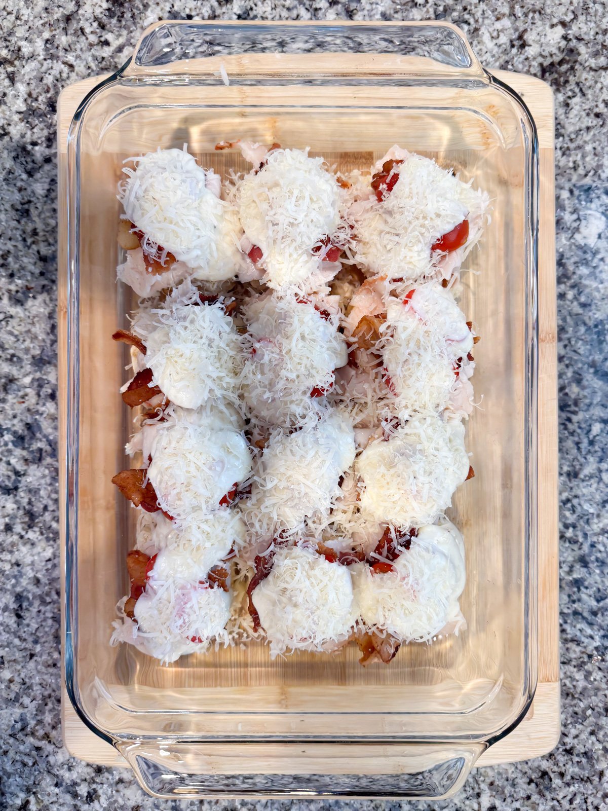 Sprinkling parmesan cheese on to of sliders in a baking dish.