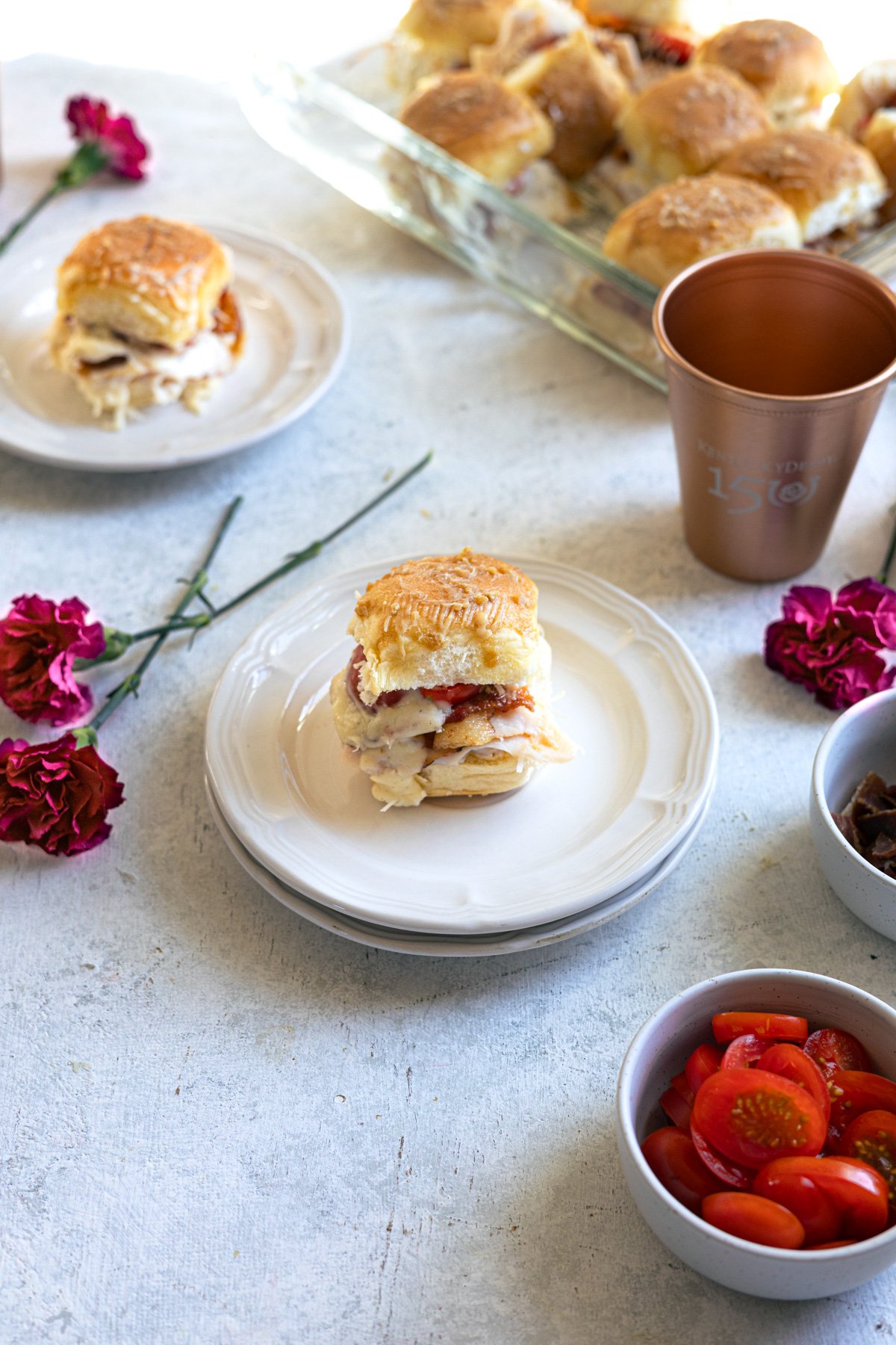 a couple small plates with a slider on it and the baking dish of the rest of the sliders behind it.