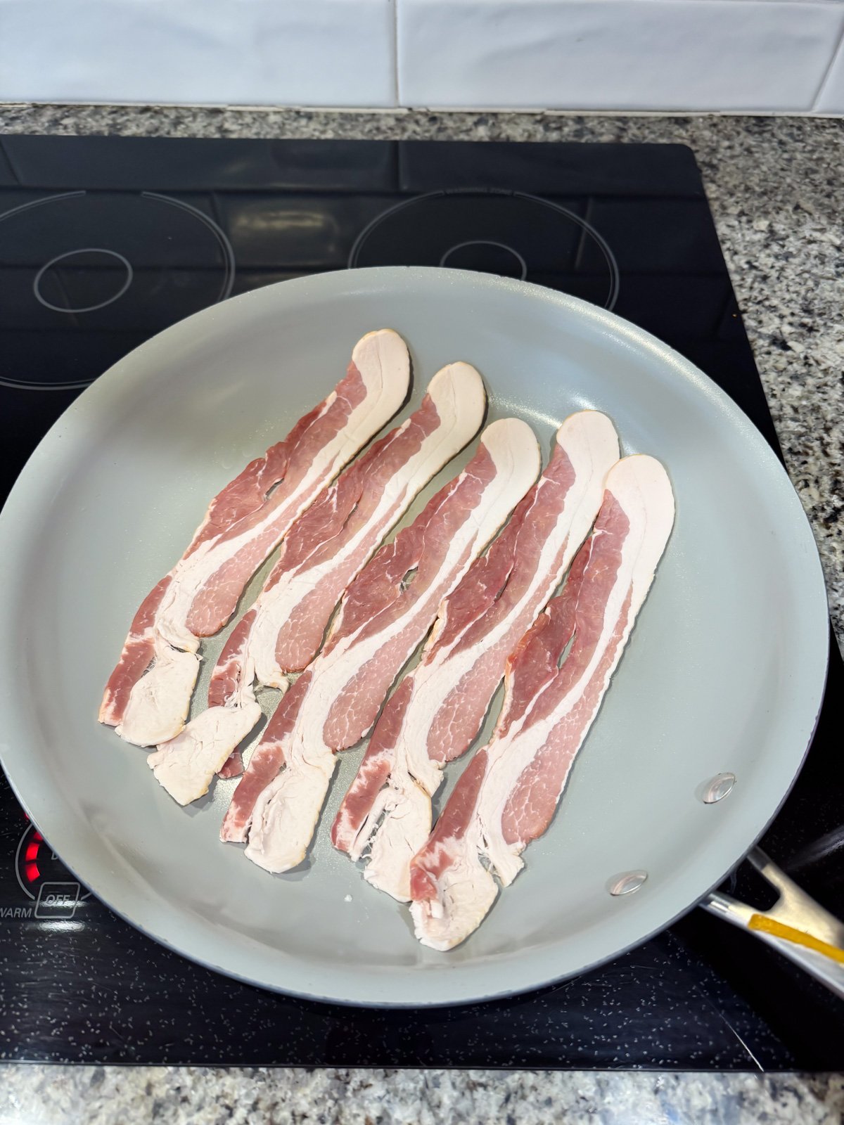 Frying up bacon in a large skillet on the stove.