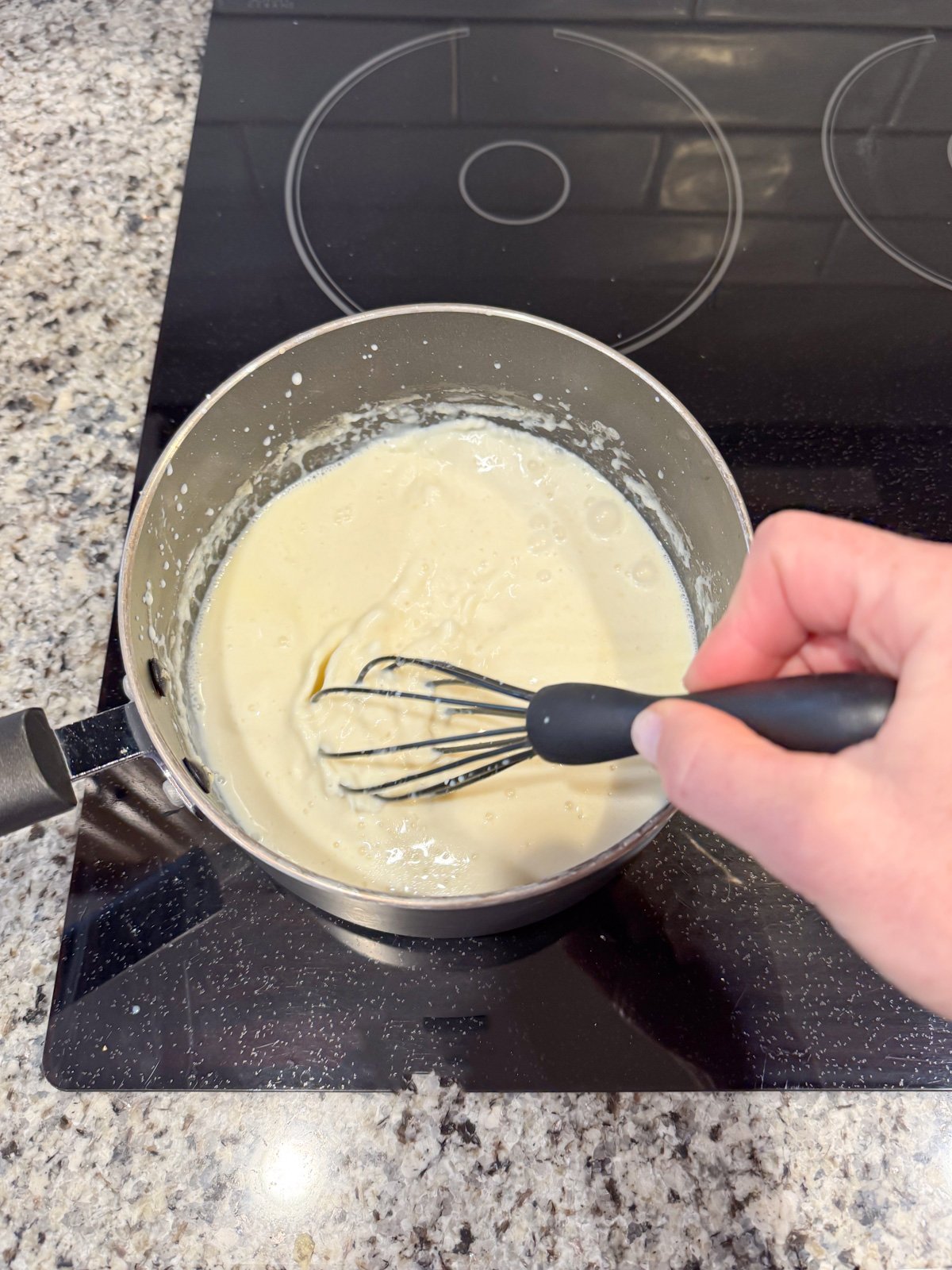 Whisking in milk to a saucepan to make a roux. 