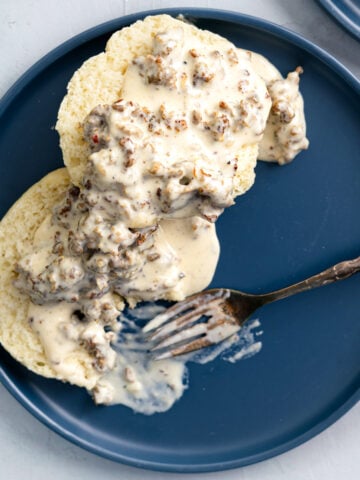 sausage gravy spooned over butter ilk biscuits with a fork eating some.