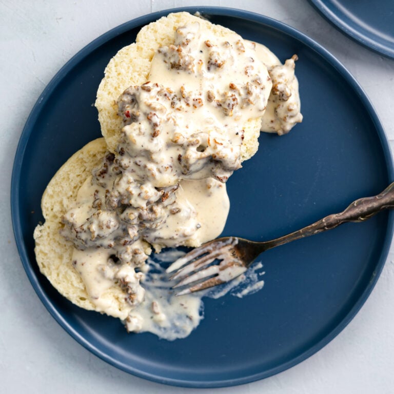 sausage gravy spooned over butter ilk biscuits with a fork eating some.