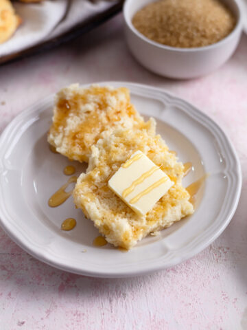 a sweet biscuit on a plate topped with butter and drizzled with honey.