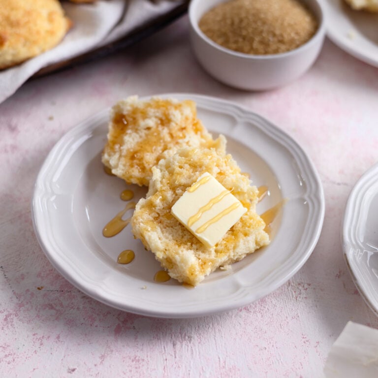 a sweet biscuit on a plate topped with butter and drizzled with honey.