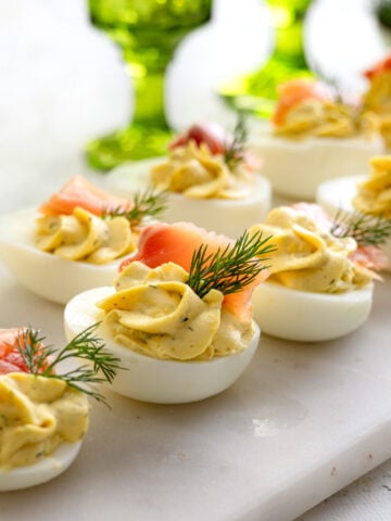 smoked salmon deviled eggs on a platter with green glasses in the background.