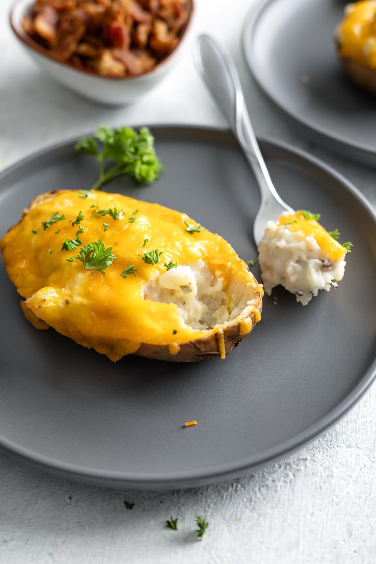 A close up of a twice baked potato on a plate with a fork taking a bite out of it.