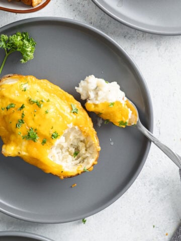 a twice baked potato on a plate with a fork taking a bite out of it.