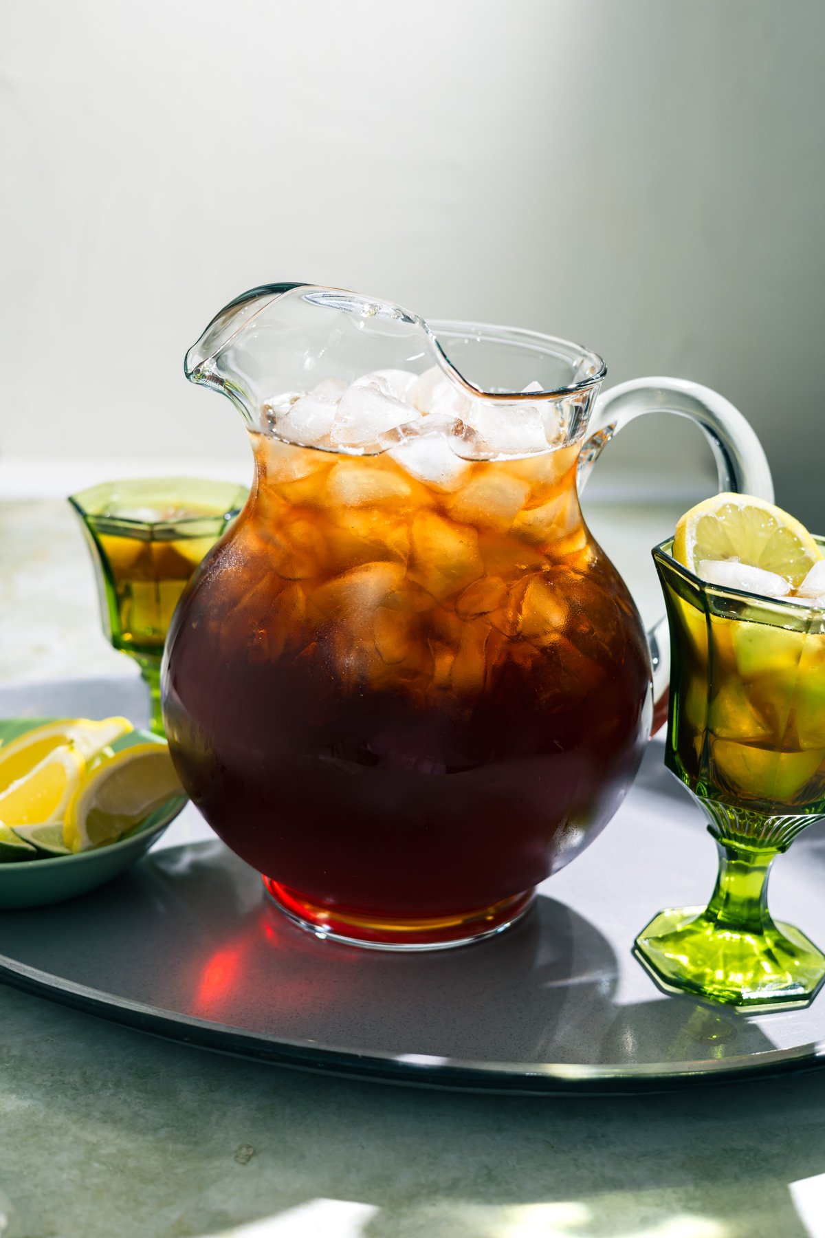 a large pitcher of sweet tea with glasses of tea behind it.