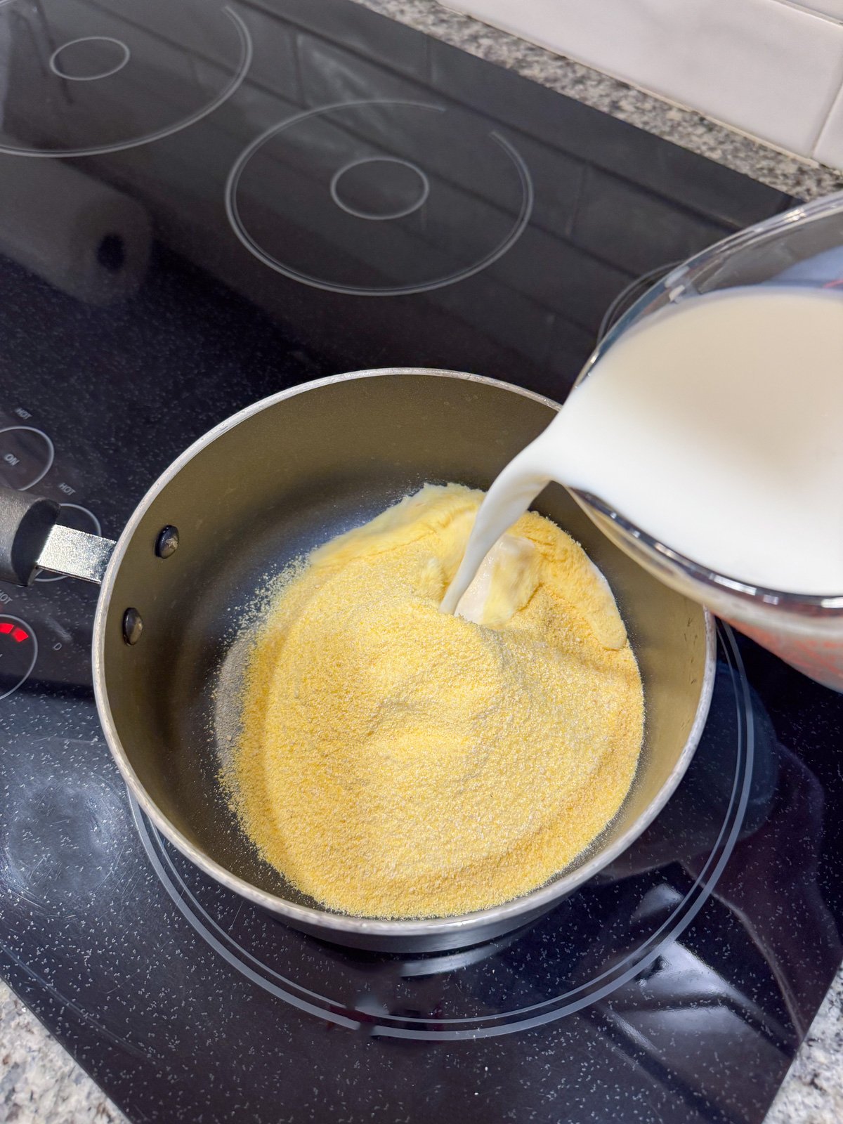 Adding milk to a pot with cornmeal.