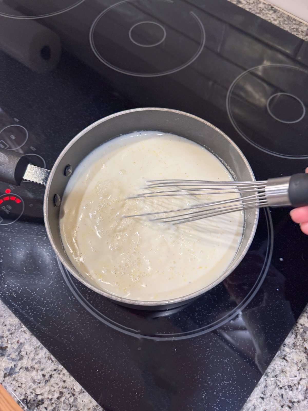 Whisking milk and cornmeal on the stove together.