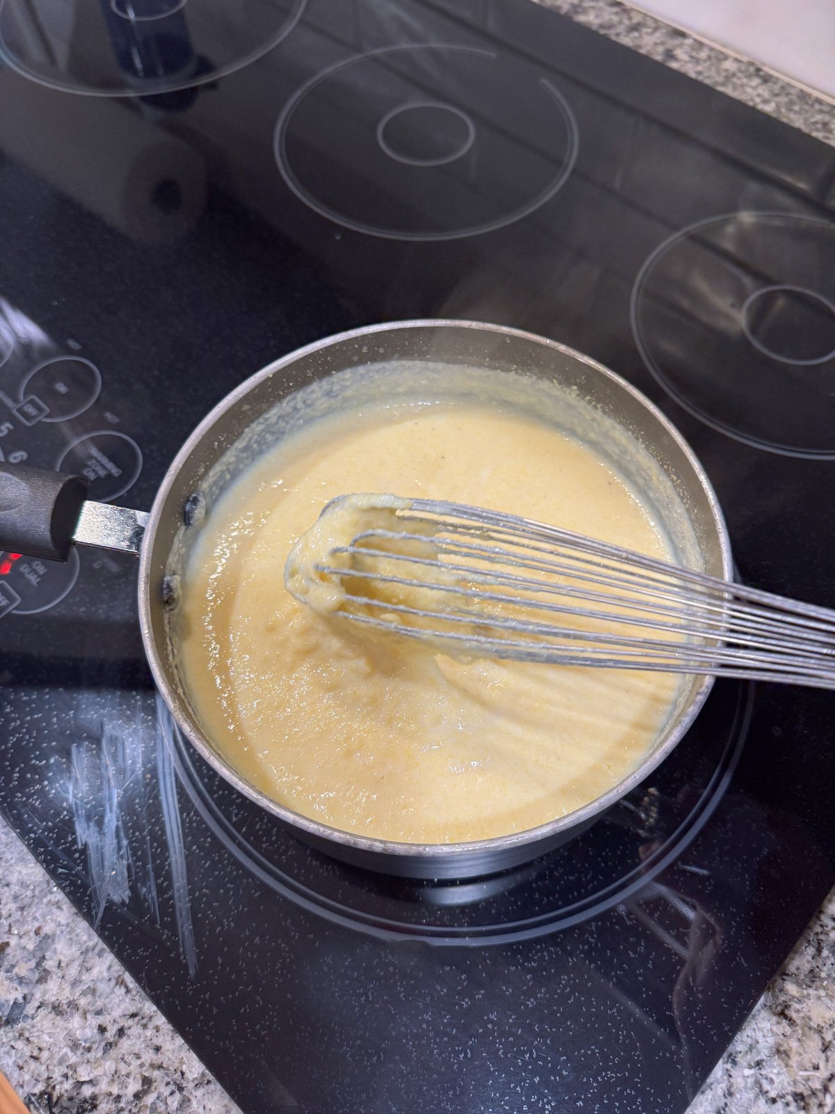 Whisking a thick cornmeal and milk mixture in ap to on the stove.