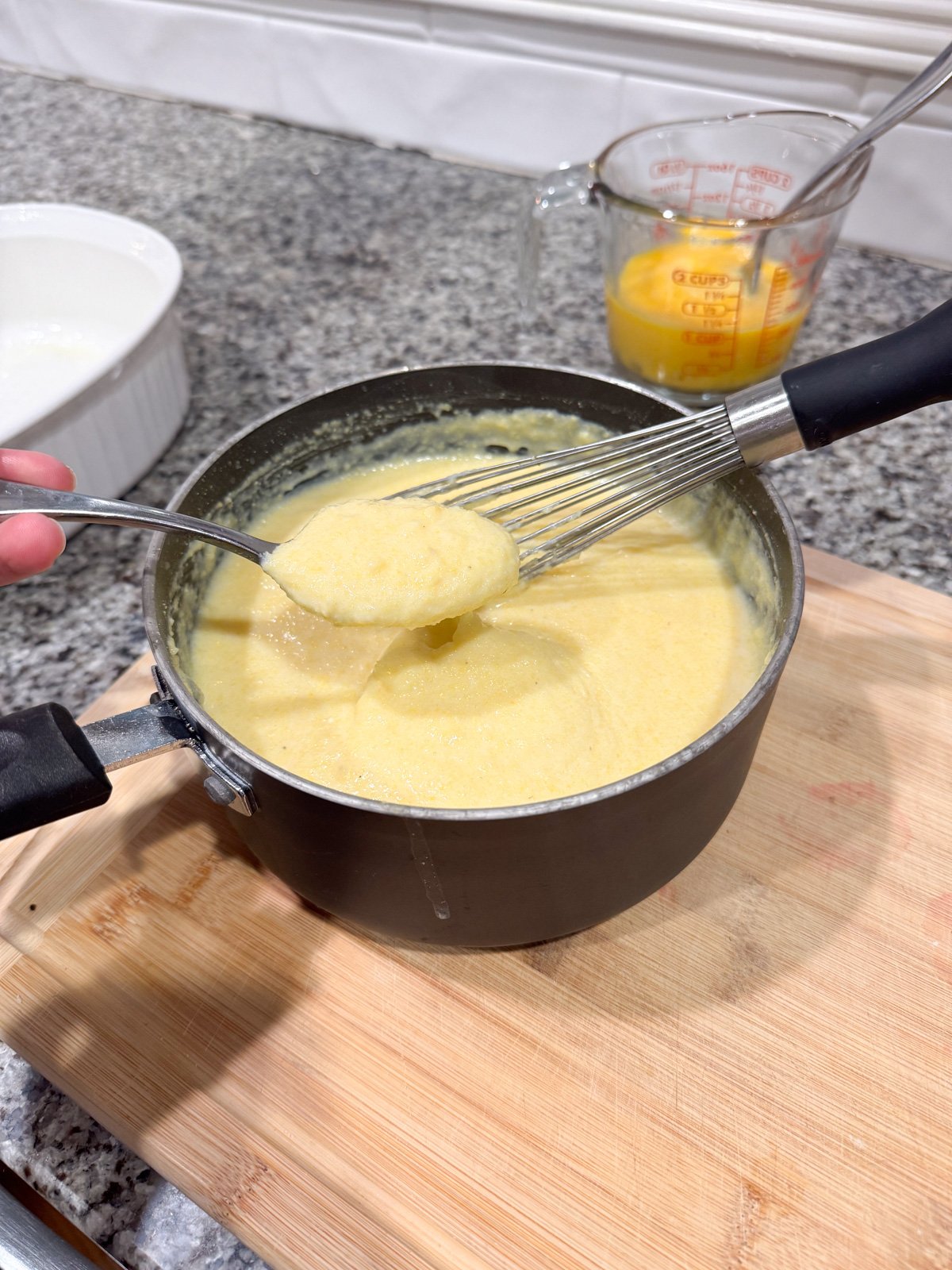 A spoon holding some spoon bread mixture cooking in a pot showing how thick it is suppose to be.