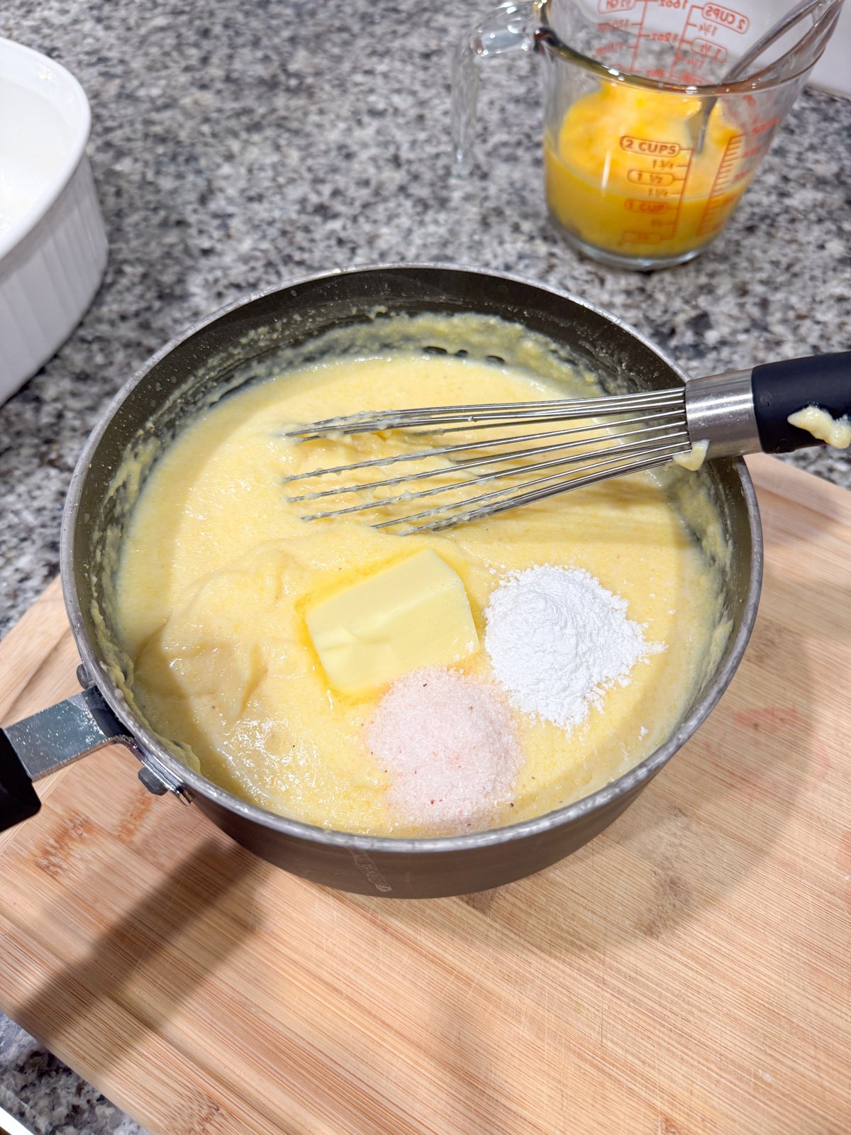 Adding butter, salt, and baking powder to a cornmeal mixture in a pot. 