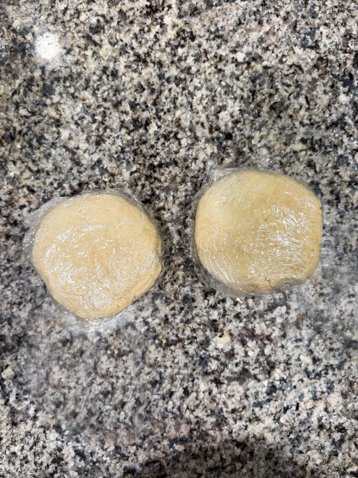 2 pie crust balls wrapped in plastic wrap.