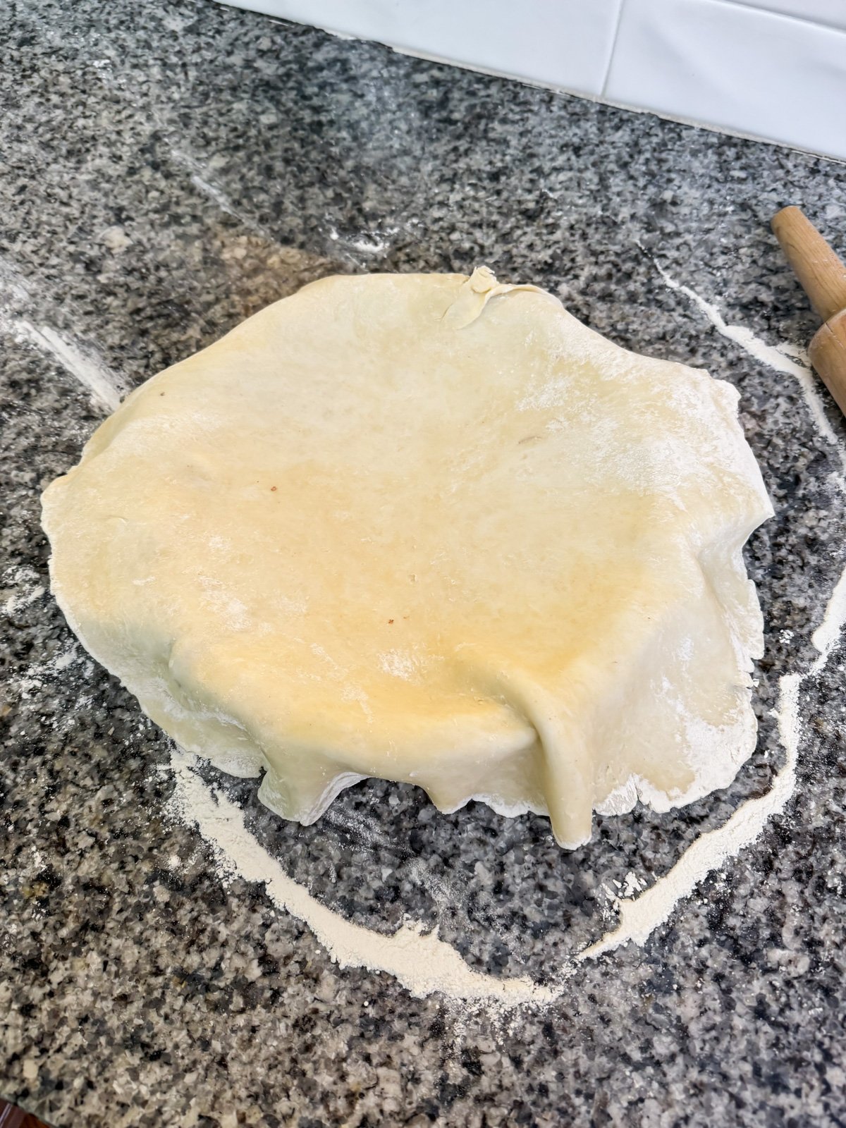 pie crust hanging over a pie plate on a kitchen counter. 