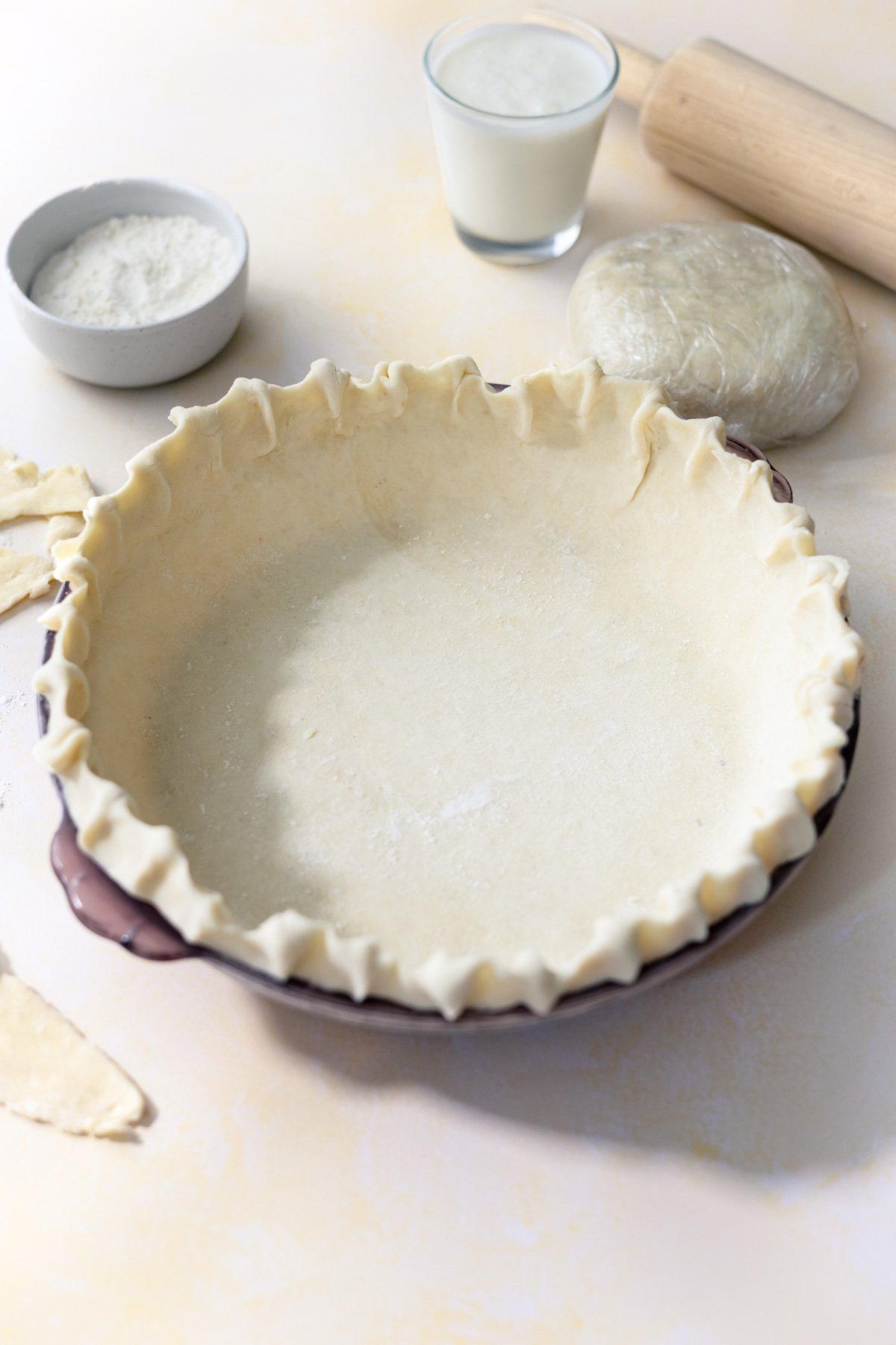 a pie crust in a pie plate with a rolling pie and flour next to it. 