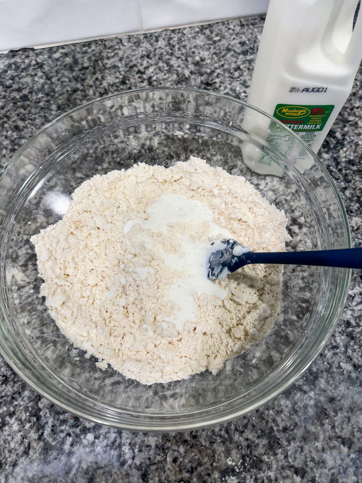 Stirring buttermilk into a flour mixture in a large bowl on a kitchen counter. 
