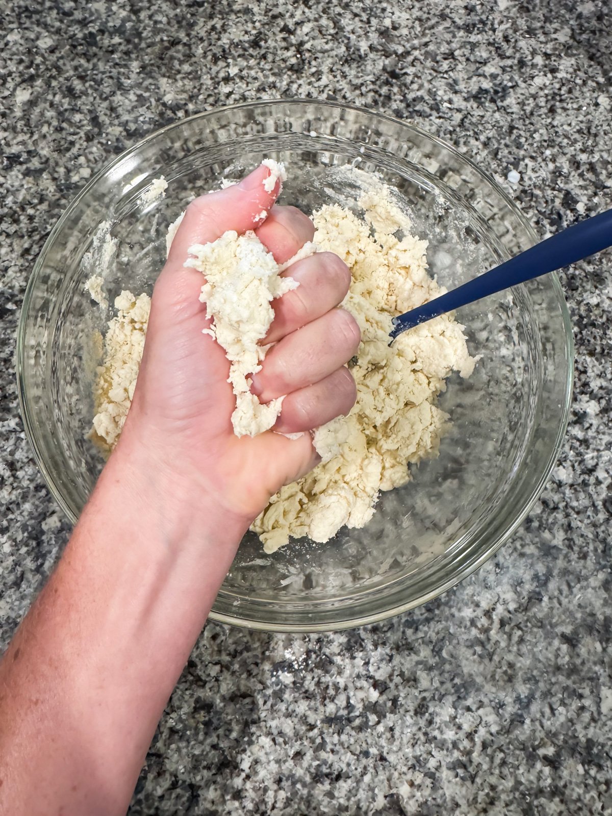a hand squeezing together pie crust dough. 