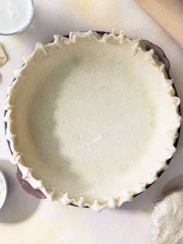 buttermilk pie crust in a pie shell with a rolling pin and flour next to it