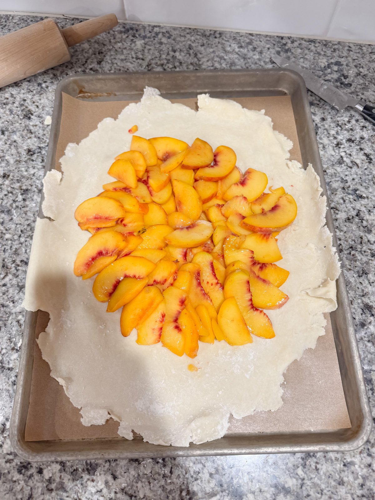 layering sliced peached on a pie crust for a peach galette.
