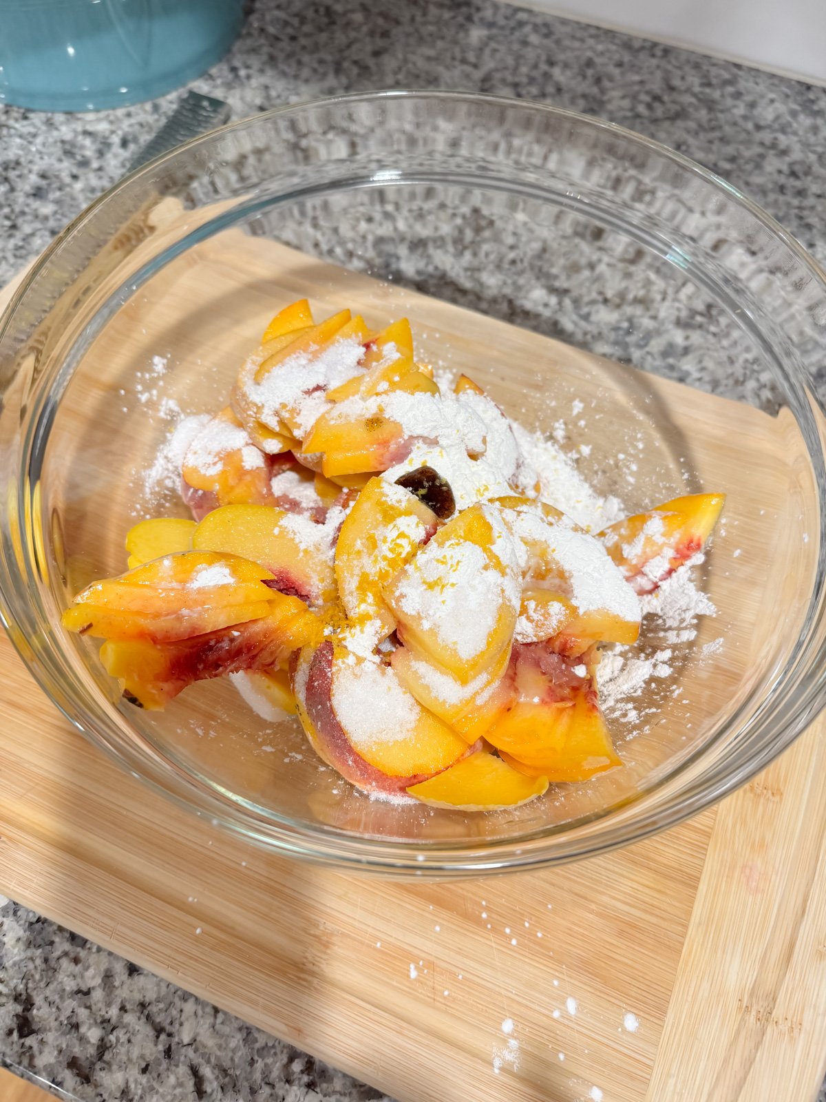 sliced peached and sugar in a mixing bowl on a kitchen counter.