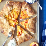 peach galette on a baking sheet with 3 pieces cut out and whipped cream next to it.