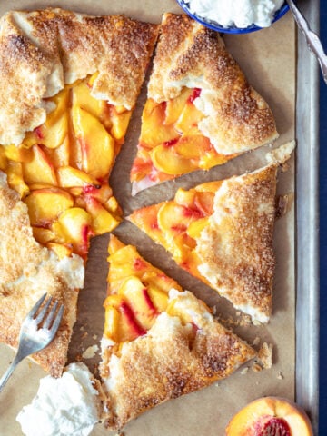 peach galette on a baking sheet with 3 pieces cut out and whipped cream next to it.
