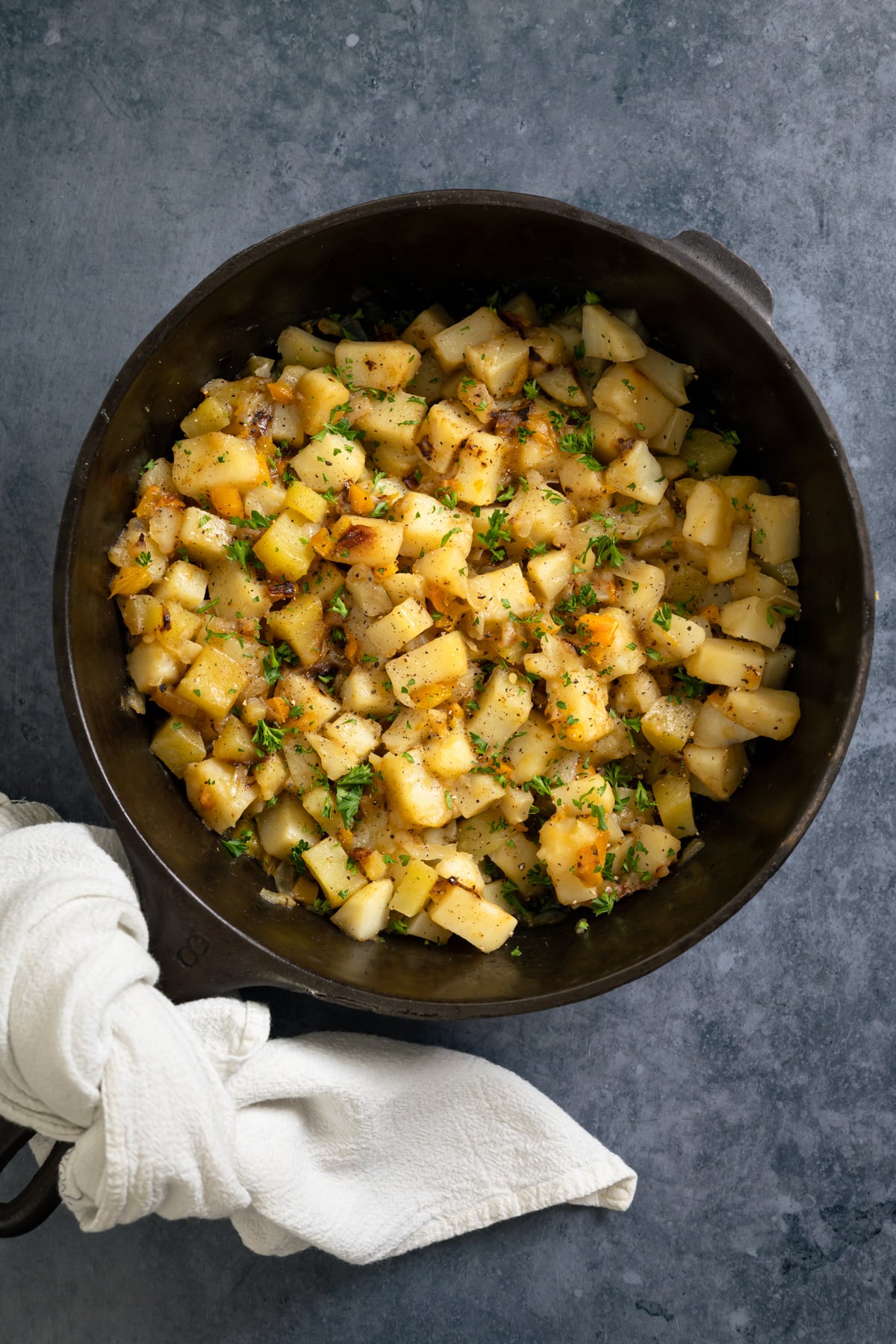 cast iron skillet full of smothered potatoes with a napkin wrapped around the handle