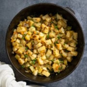 cast iron skillet full of smothered potatoes with a napkin wrapped around the handle