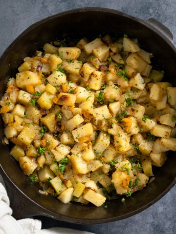cast iron skillet full of smothered potatoes with a napkin wrapped around the handle
