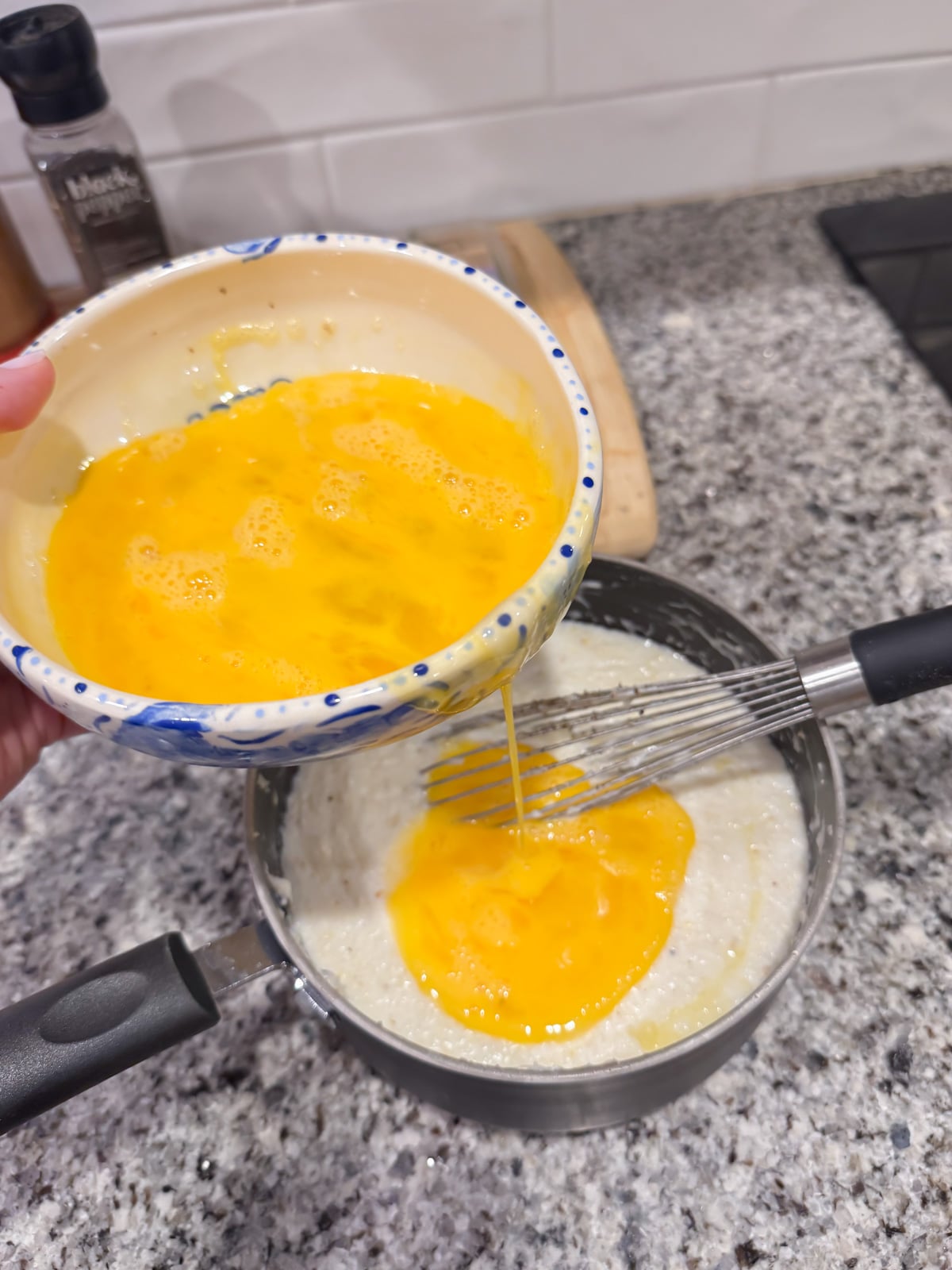 Slowly adding whisked eggs into cooked grits in a pot.