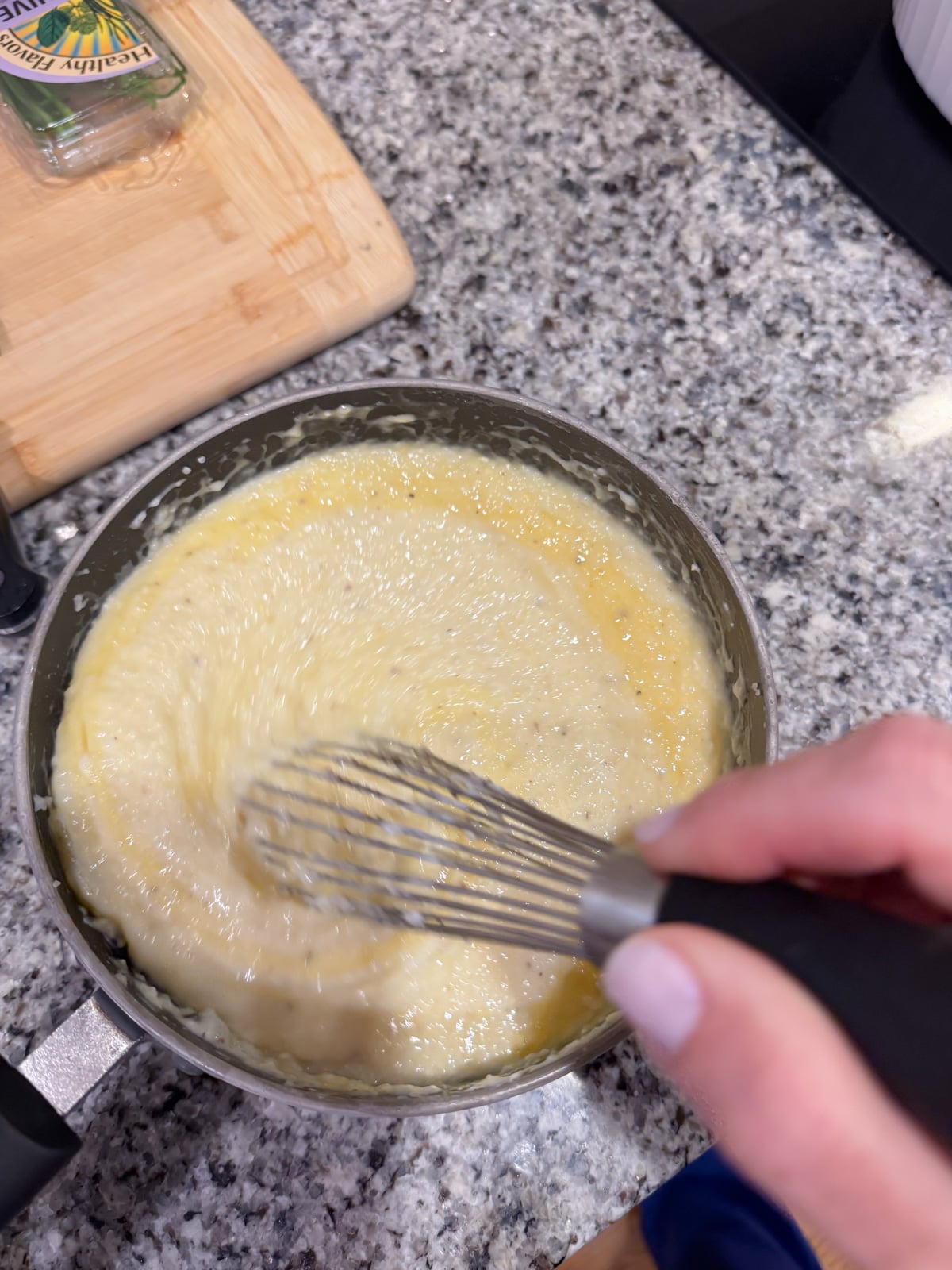 Whisking in cheese into a pot of grits on top of a counter.