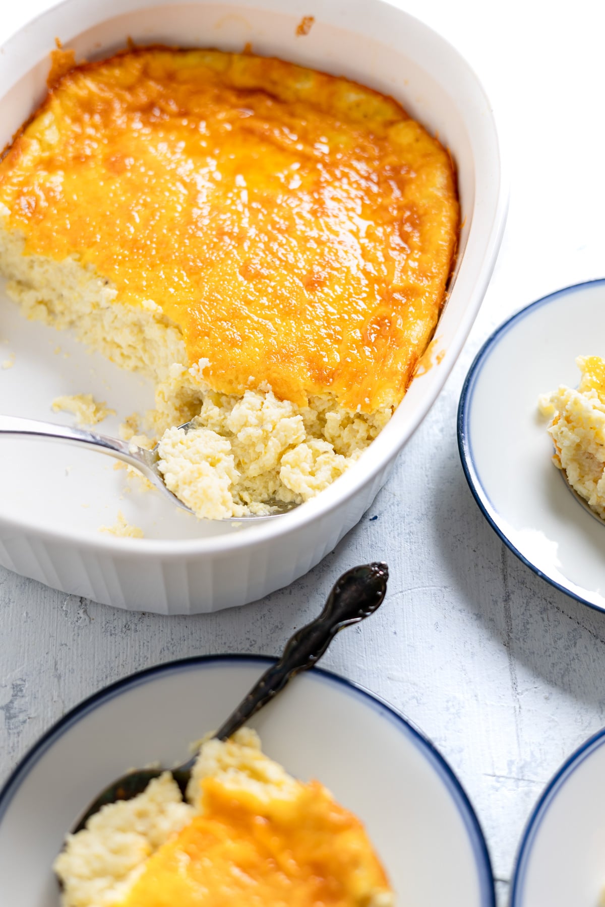 Scooping our servings of baked cheddar grits casserole on small plates.