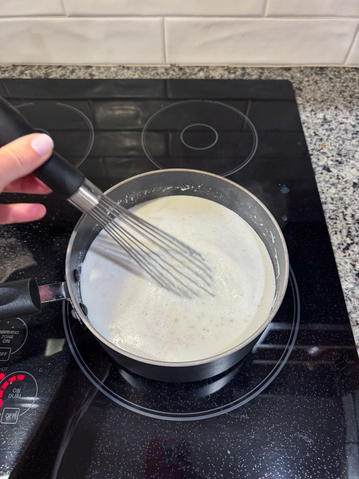 Whisking grits cooking in a pot on the stove.