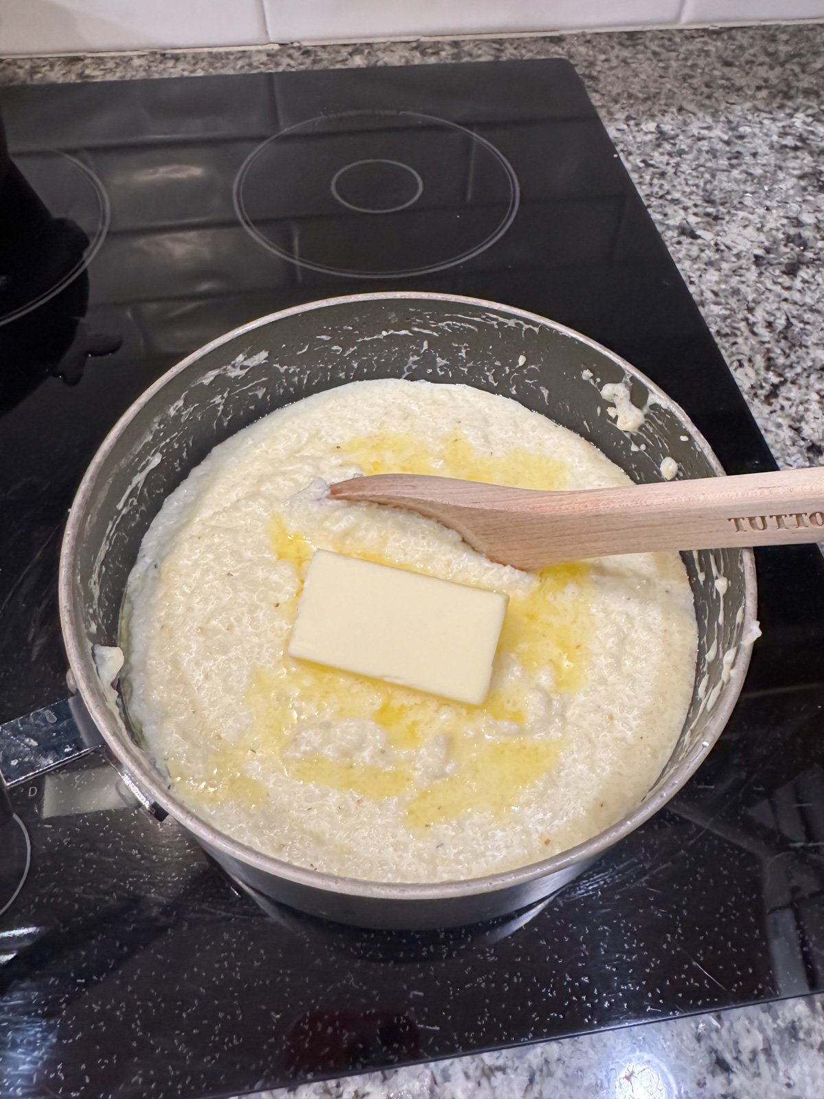 Stiring in butter to cooked grits in a pot.