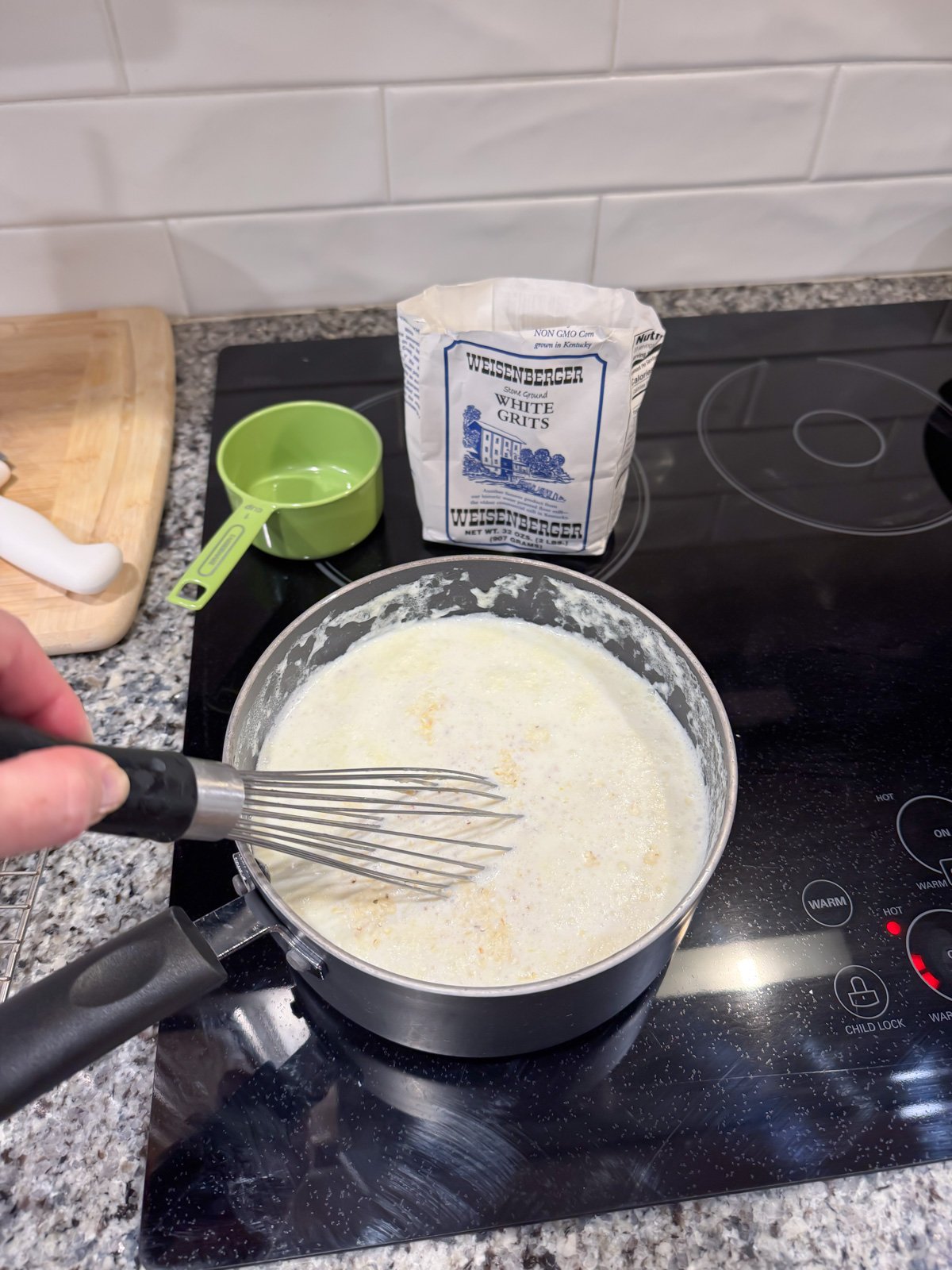 whisking in grits to milk that's cooking on the stove.