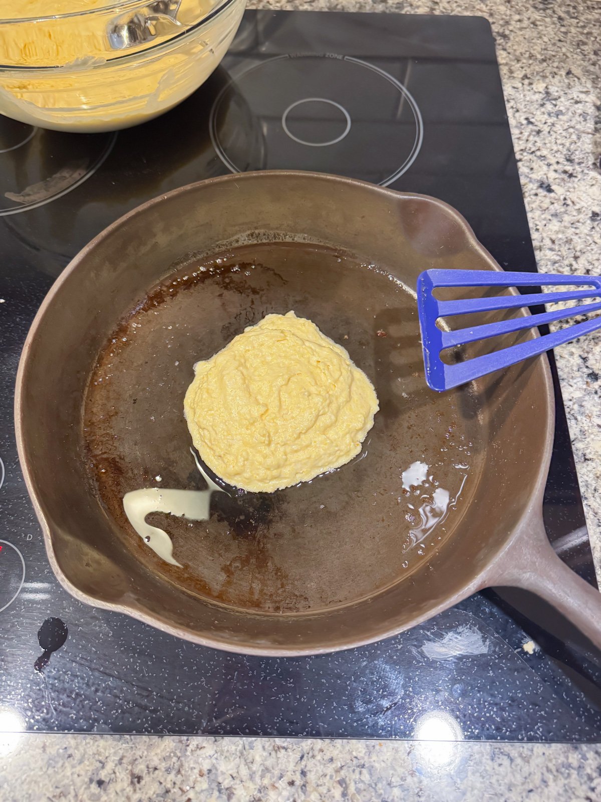 frying up a hoe cake in a cast iron skillet on the stove.