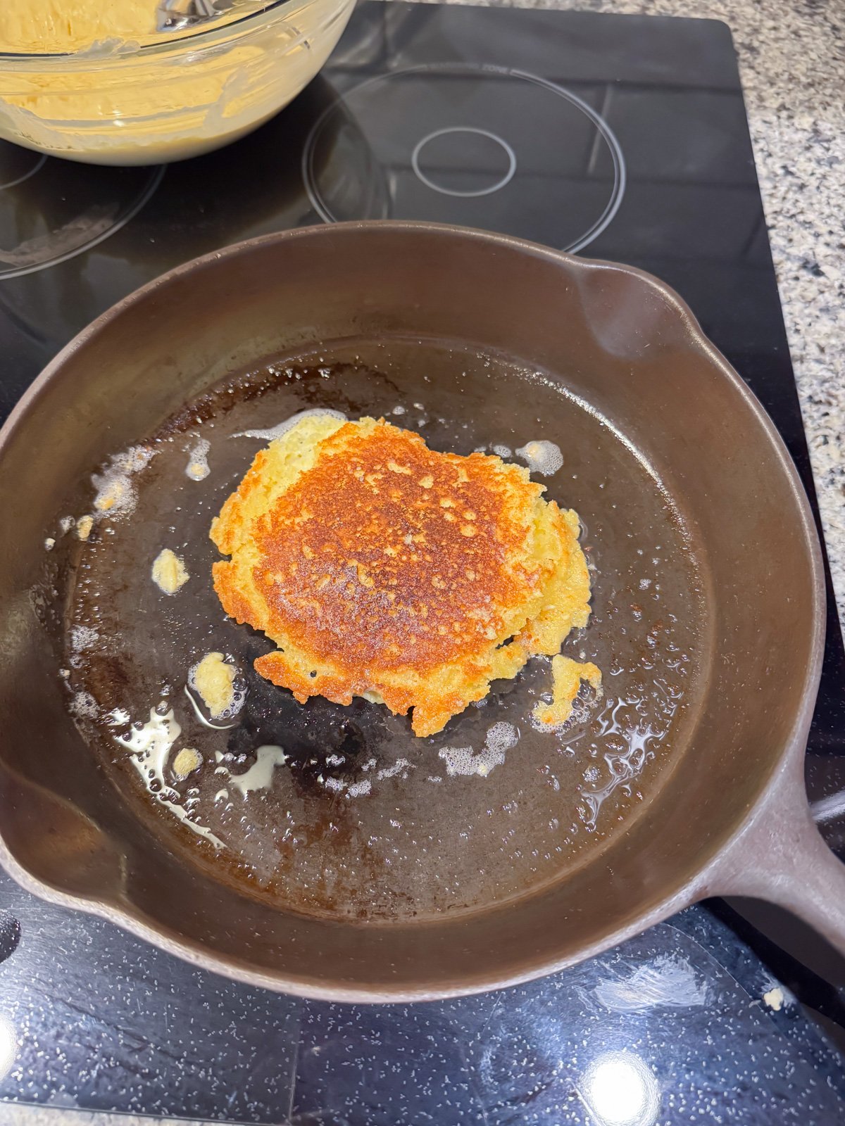 frying up a hoe cake in a cast iron skillet on the stove.