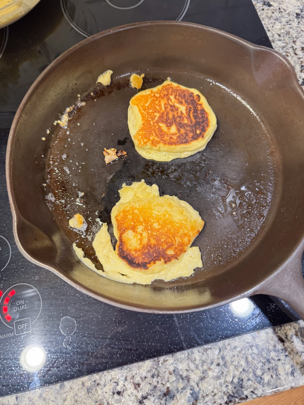 frying up a 2 hoe cakes in a cast iron skillet on the stove.
