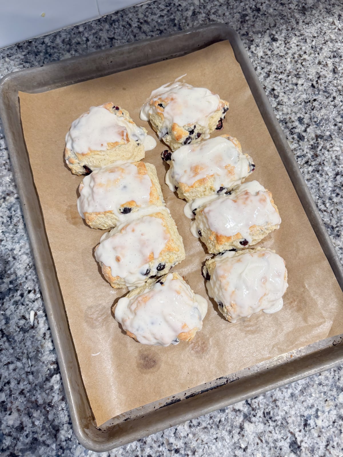 Glazing the top of blueberry biscuits with a vanilla glaze on a baking sheet.