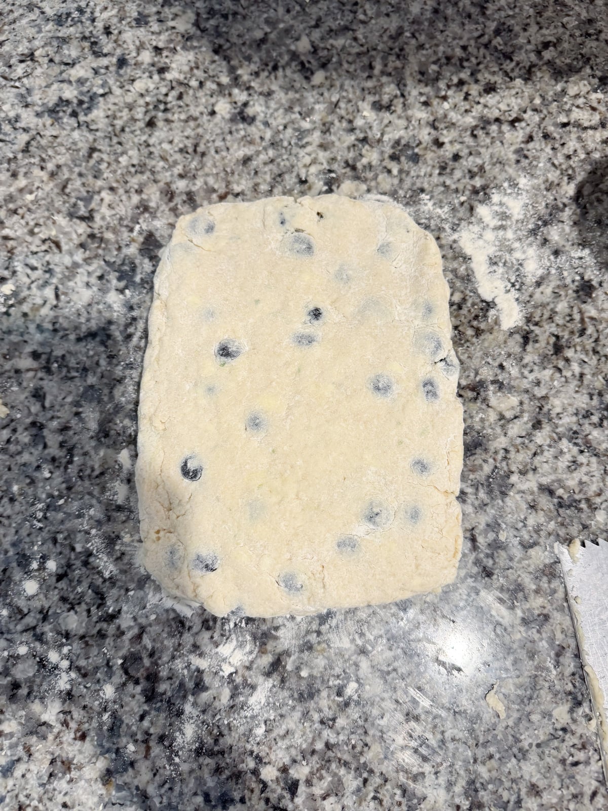 Shaping blueberry biscuit dough into a triangle on a counter.