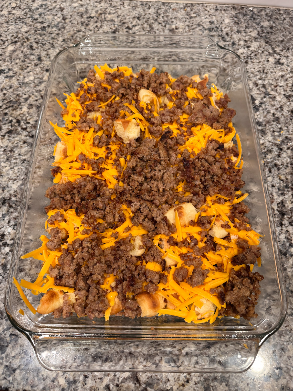 A baking dish with croissants, cheese and sausage.