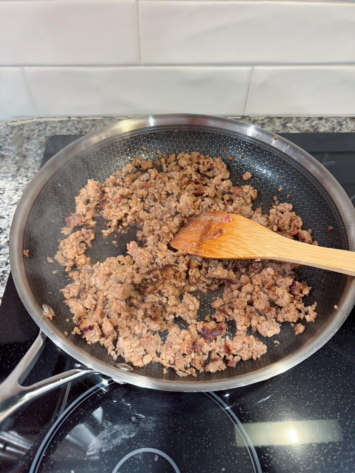 Cooking sausage in a large skillet with a wooden spoon.