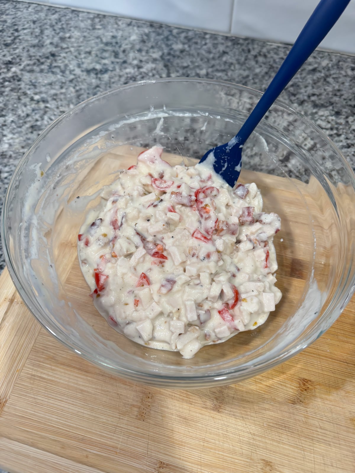 Stirring together a turkey and sauce mixture with a blue spatula in a large bowl on a cutting board.