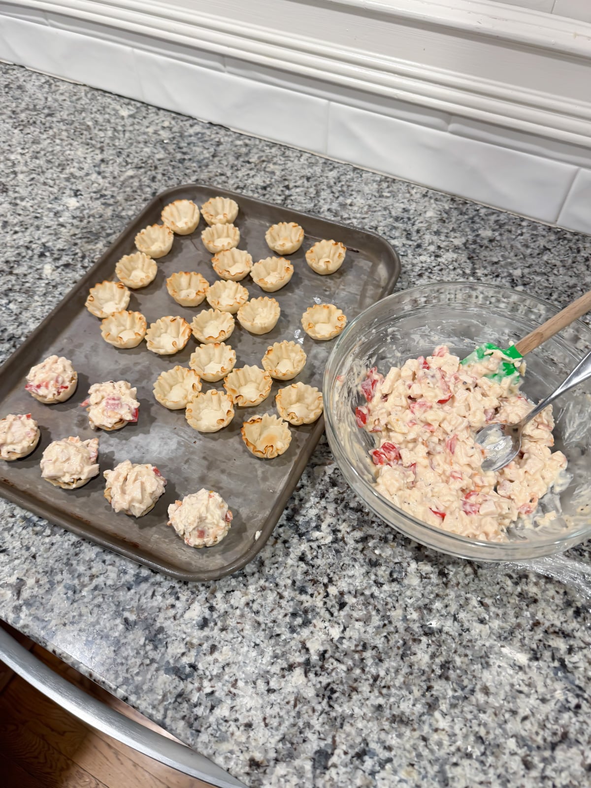 Scooping a hot brown mixture into phyllo shells on a baking tray.