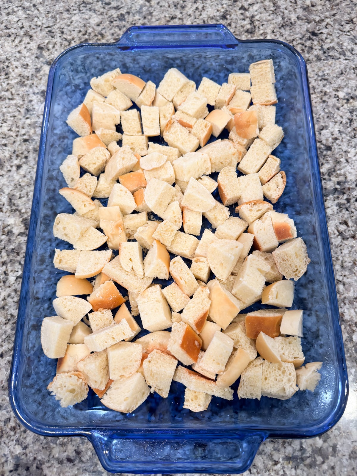 Cubed sourdough bread spread out evenly in the bottom of a 9x13 baking dish.
