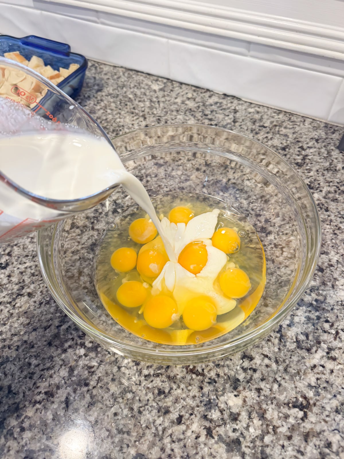 pouring milk into a large mixing bowl with eggs.