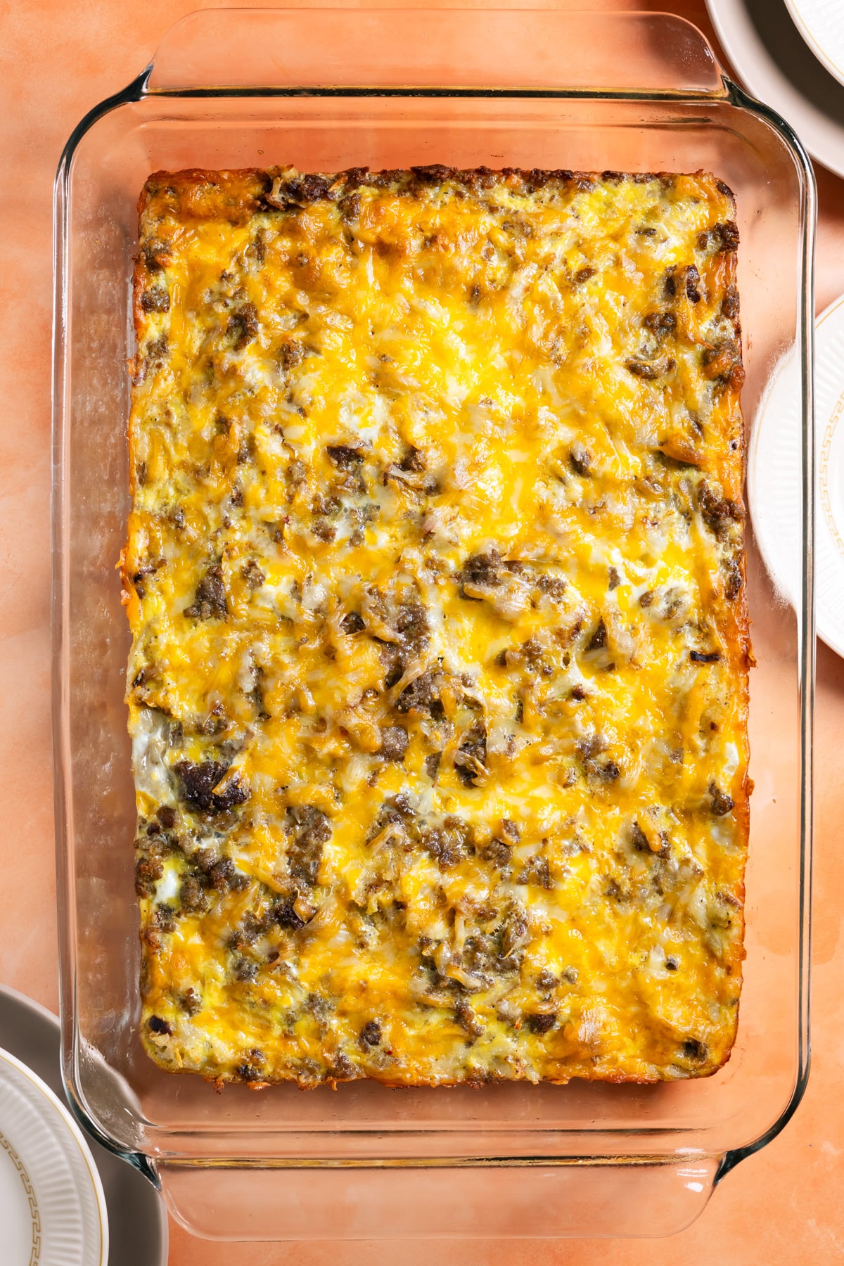 sausage hash brown breakfast casserole in a baking dish right after coming out of the oven on an orange background.