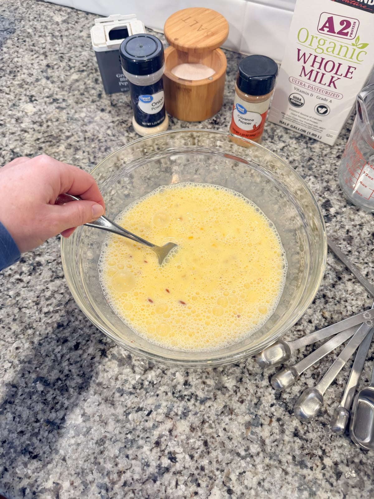 whisking together an egg and milk mixture in a large bowl for a breakfast casserole.